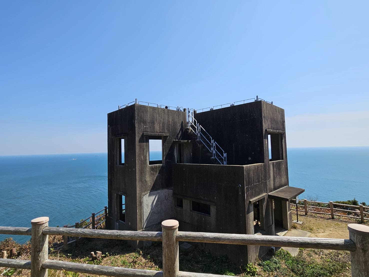 山道の先に現れる監的哨跡。背景には青空と海が広がっている。